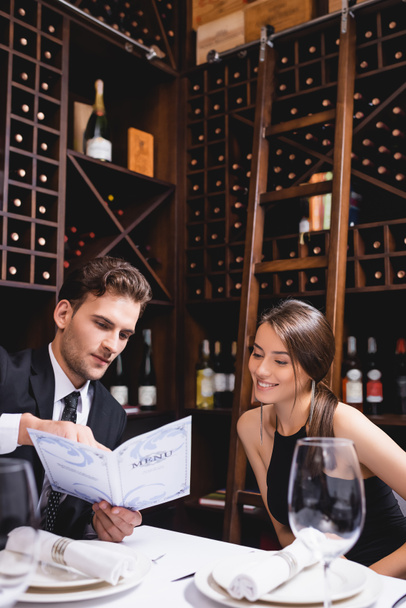 Selectieve focus van elegante man holding menu in de buurt van vriendin in restaurant  - Foto, afbeelding