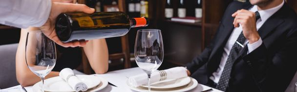 Ιστοσελίδα κεφαλίδα του σομελιέ ρίχνει κρασί σε ποτήρι κοντά ζευγάρι στο εστιατόριο  - Φωτογραφία, εικόνα