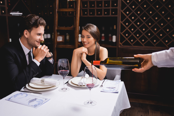 Selective focus of young couple sitting near sommelier pouring wine in glass in restaurant  - Фото, изображение