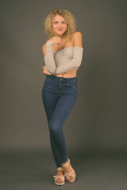 Studio shot of young beautiful woman with blond curly hair against gray background - Fotografie, Obrázek