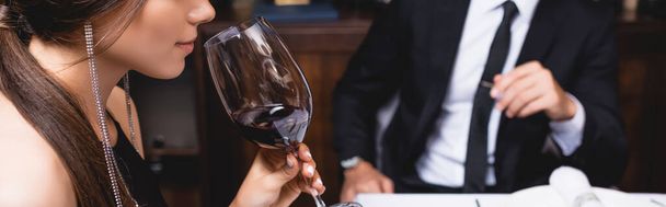 Encabezado del sitio web de mujer joven oliendo vino en vidrio cerca de hombre  - Foto, Imagen