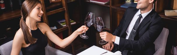 Panoramic orientation of elegant couple clinking with wine in restaurant  - Valokuva, kuva