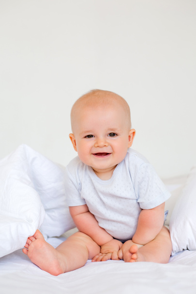 6 aylık neşeli bir erkek bebeğin beyaz bir bedenle yatakta fotoğrafı.  - Fotoğraf, Görsel