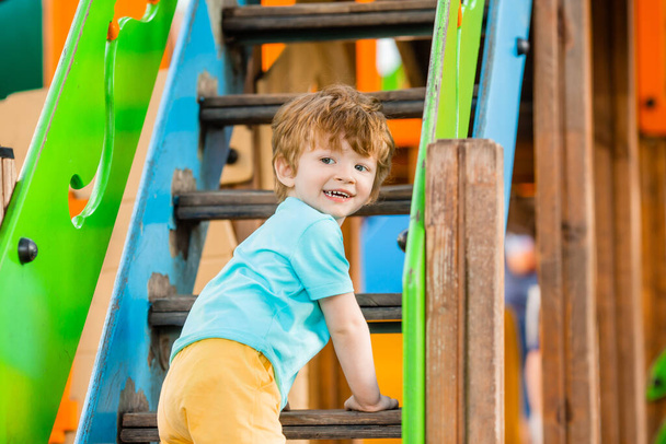 Wesoły rudzielec bawi się na kolorowym zjeżdżalni i wspinaczka plac zabaw wieża - Zdjęcie, obraz