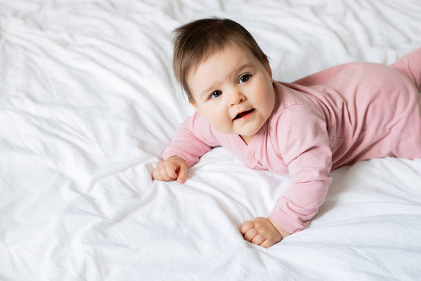 Photo of toddler girl in pink jumpsuit lying in crisp white bed  - Fotoğraf, Görsel