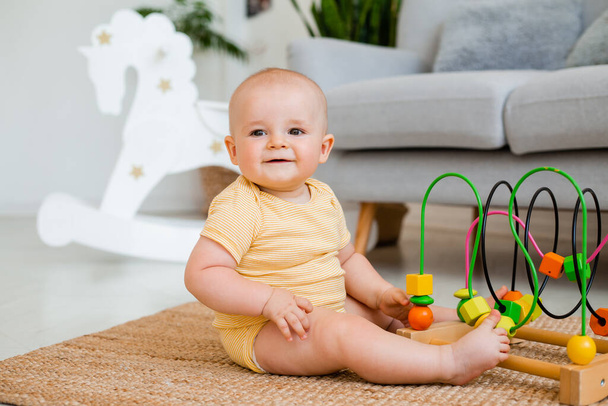 Niedliches Kleinkind im gelb gestreiften Body sitzt mit Entwicklungsspielzeug auf dem Teppich. Entwicklungskonzept für Kinder - Foto, Bild