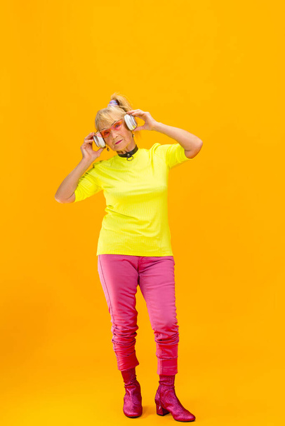 Senior woman in ultra trendy attire isolated on bright orange background - Фото, изображение