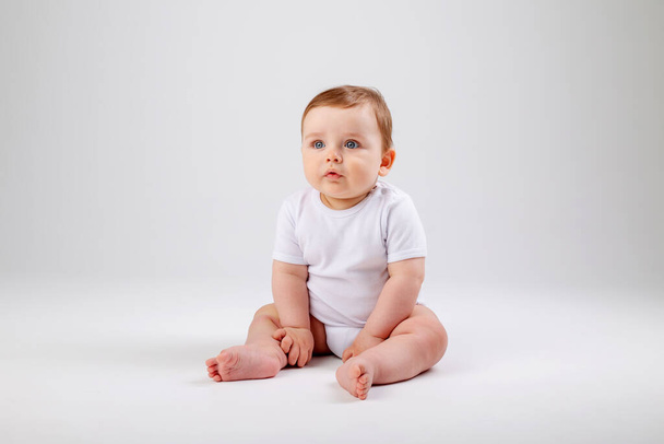 Cute toddler boy in white bodysuit sits still. Isolated image on white background - Φωτογραφία, εικόνα
