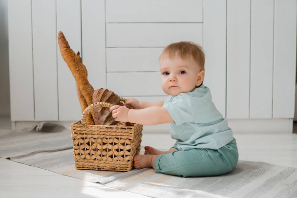 Малыш в мяте сидит на кухне с корзиной свежего хлеба. - Фото, изображение
