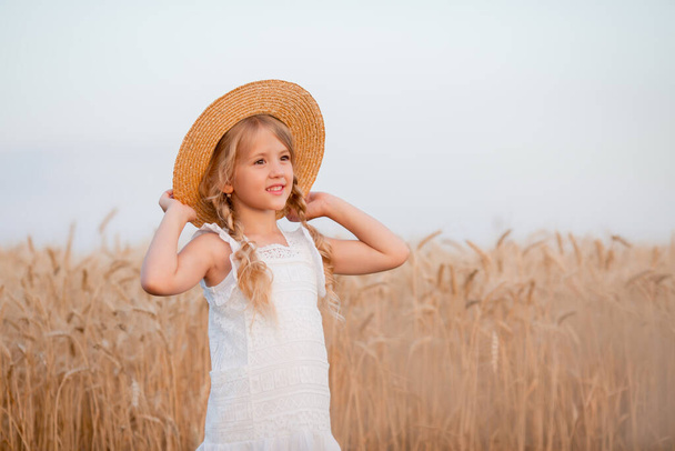 Kuva pieni blondi tyttö olki hattu ja valkoinen mekko kesällä vehnäpellolla. Luonnon- ja ekoelämän käsite - Valokuva, kuva