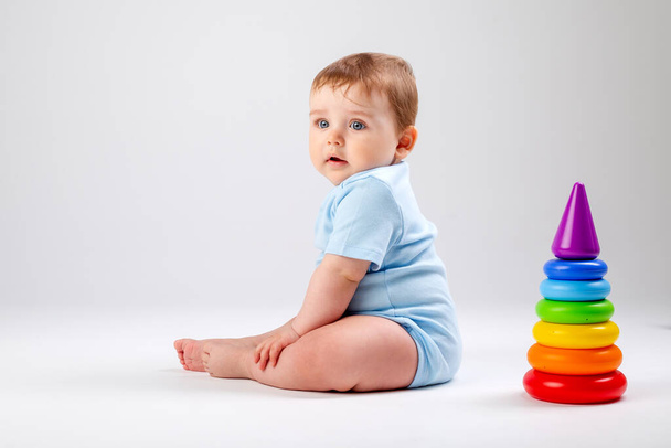 Bebê bonito em azul bodysuit brinca com pirâmide multicolorida. Imagem isolada sobre fundo branco - Foto, Imagem