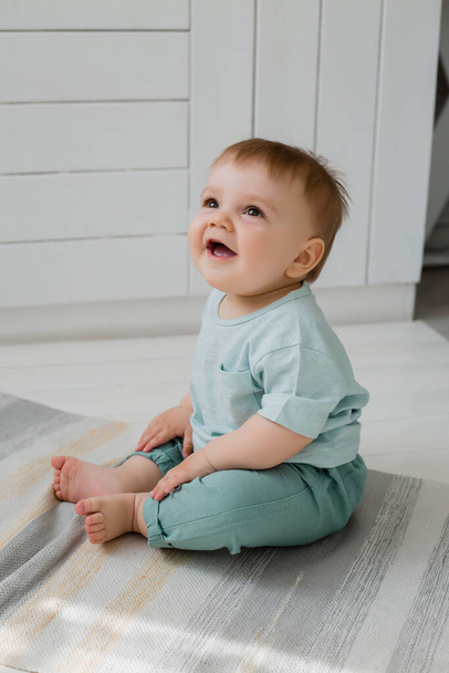 Toddler boy in mint colored clothes sits on kitchen floor - Fotografie, Obrázek