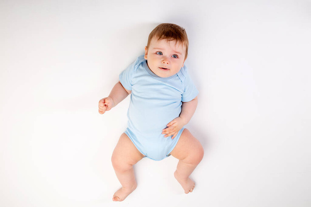 Симпатичный мальчик 8 месяцев в синем купальнике сидит на белом фоне, место для текста - Фото, изображение