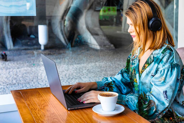 Retrato de una joven en la cafetería que está trabajando en el ordenador portátil en una cafetería. La mujer bebiendo un café - Foto, imagen