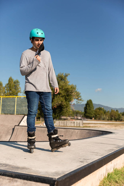 катающийся на роликах мужчина в футболке, защитном шлеме и противовирусной маске (новая постковидная нормальность) в скейт-парке - Фото, изображение