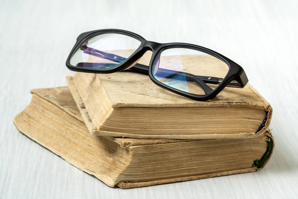 Eyeglasses on stacked books placed on white wooden background - Foto, afbeelding