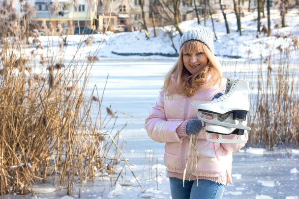 девушка в зимней одежде и шляпе с фигурными коньками на фоне замерзшего озера, тема здорового образа жизни и активного отдыха зимой, вид сзади, место для текста - Фото, изображение