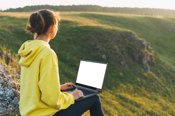 Crop fénykép fiatal nő utazó szabadúszó sárga kapucnis fehér képernyős nyitott laptop gyönyörű kilátás háttér, mock up - Fotó, kép