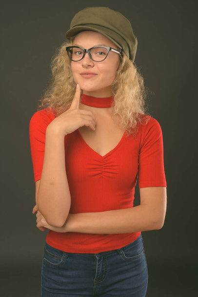 Studio shot of young beautiful woman with blond curly hair against gray background - Photo, Image