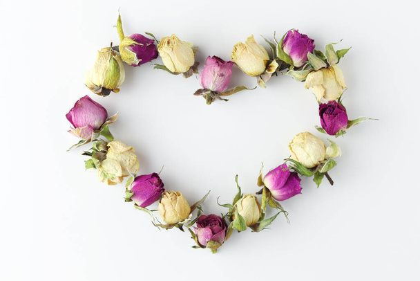Φθινοπωρινή σύνθεση. Καρδιά σύμβολο φτιαγμένο από αποξηραμένα φθινοπωρινά λουλούδια και φύλλα σε λευκό φόντο. Πάνω άποψη, επίπεδη lay - Φωτογραφία, εικόνα