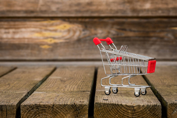 Small shopping cart on wheatered wood background - Фото, изображение