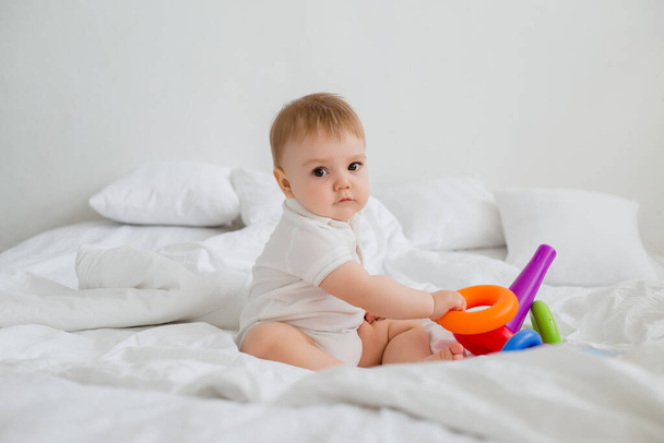 Симпатичный ребенок играет с красочной пирамидой радуги игрушки на белой кровати - Фото, изображение