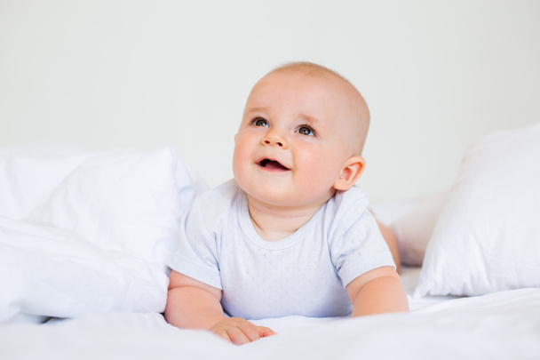 6ヶ月の明るい赤ん坊の男の子の写真でベッドの中の白いボディスーツ  - 写真・画像