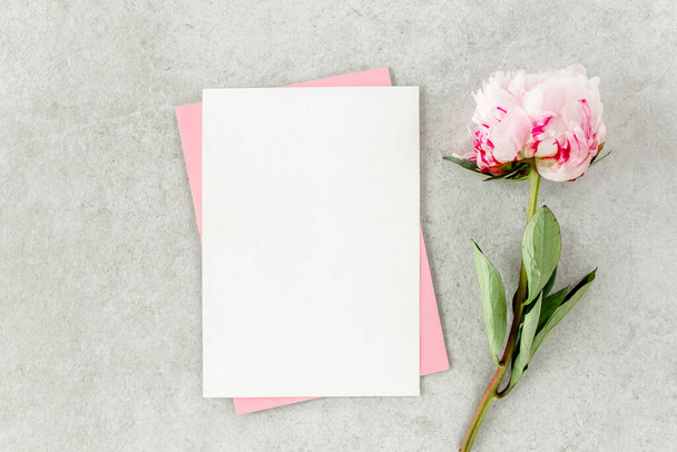 Mockup invitation, blank paper greeting card, pink envelope and peonies on gray stone table. Flower background. Flat lay, top view. - Foto, immagini