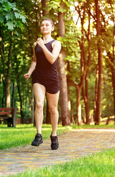 Sporty young woman running by road in the summer city park. - Foto, Bild