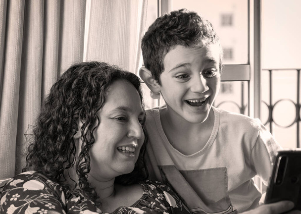 Braziliaanse moeder en zoon glimlach zien smartphone samen - Foto, afbeelding