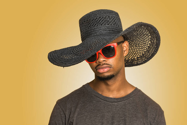若いですアフリカ系アメリカ人男で女性的な帽子とスタイリッシュなサングラスに対する黄色の背景 - 写真・画像