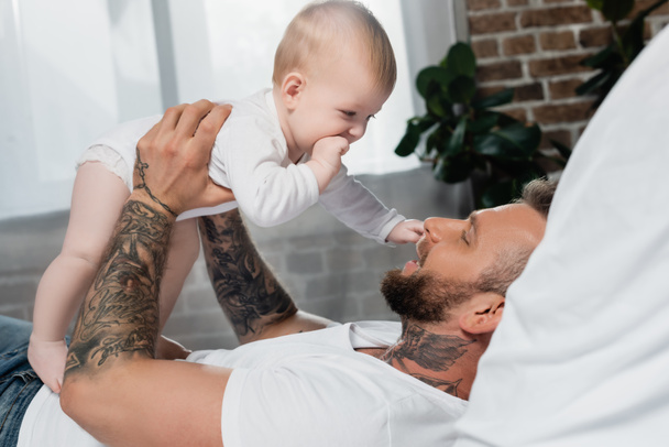 side view of young father holding infant kid while lying in bed - Photo, Image
