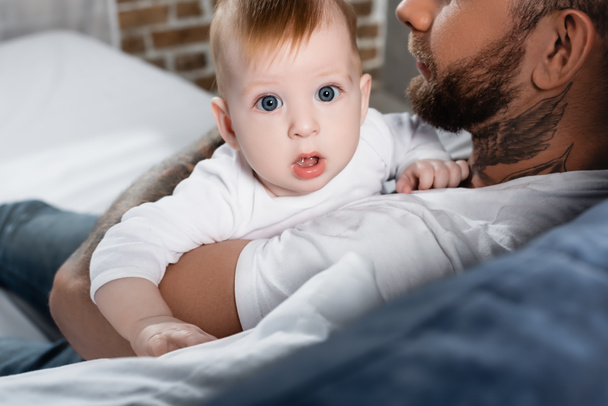 селективный фокус ребенка, смотрящего в камеру с открытым ртом в руках отцов - Фото, изображение