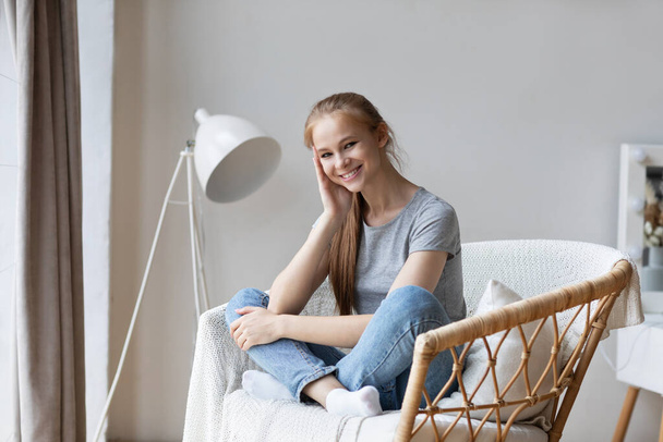 Young happy woman sitting on modern chair enjoying morning at home. Good weekend. - Foto, immagini