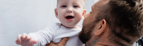 selective focus of young father holding excited baby boy looking at camera with open mouth, panoramic concept - Fotoğraf, Görsel