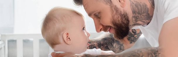 horizontal image of young tattooed man and infant son looking at each other face to face - Photo, Image