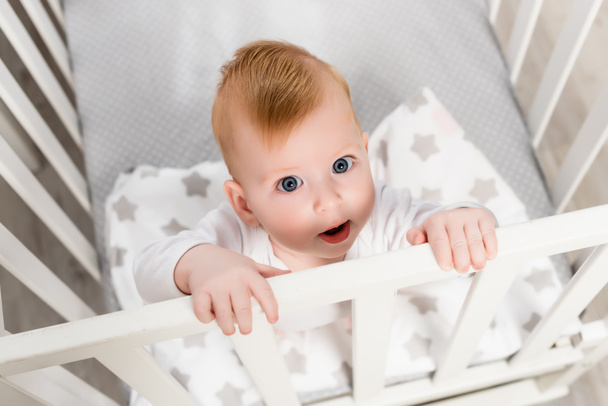 overhead view of infant boy looking at camera while standing in crib - Fotoğraf, Görsel