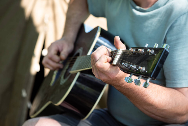 Dışarıda çadırın yanında gitar çalan bir adam. Elleri yakınlaştırın. Kamp, turistik hayat, romantizm. Seçici odaklanma. Yaz tatili kavramı - Fotoğraf, Görsel