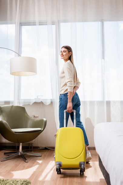 young woman standing with yellow baggage in hotel room - Foto, Imagem