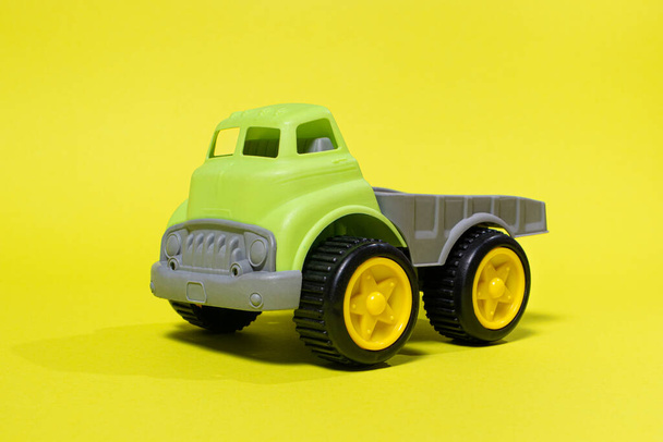 Speelgoedauto op een gele achtergrond - bouwmateriaal voor kinderen. Heldere kinderen plastic speelgoed, dumpen truck jeugd. - Foto, afbeelding