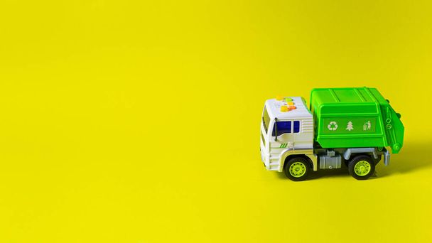 おもちゃは、おもちゃ店のテキストのための場所と黄色の背景バナーに白いボディを持つゴミ収集車の緑です。子供のおもちゃタイプライター. - 写真・画像