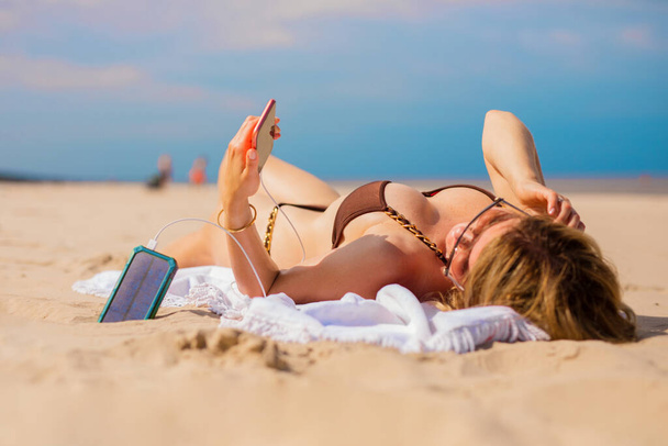 Frau lädt Handy am Strand mit tragbarem Solarakku auf - Foto, Bild