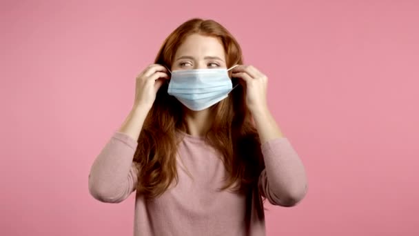 Jeune jolie femme met sur le visage masque médical pendant la pandémie de coronavirus. Portrait sur fond rose. Protection avec respirateur contre l'éclosion de COVID-19 - Séquence, vidéo
