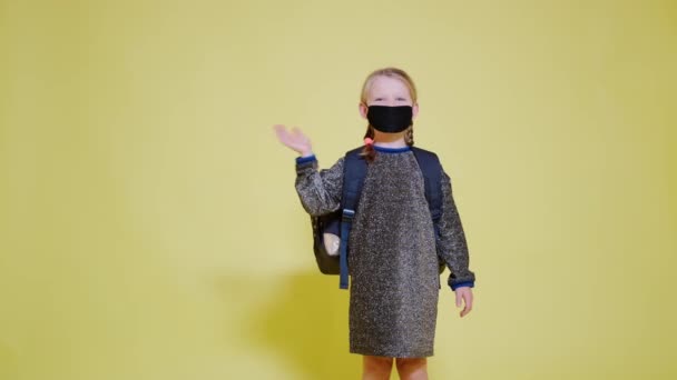 schoolmeisje dragen van een medisch masker maakt het teken van groet en gaat weg  - Video