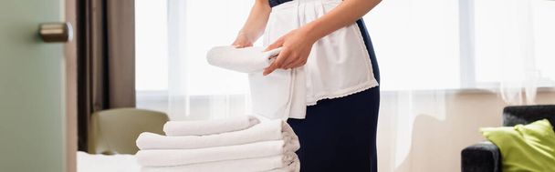 vista cortada da empregada em avental segurando toalha limpa no quarto do hotel, tiro panorâmico - Foto, Imagem