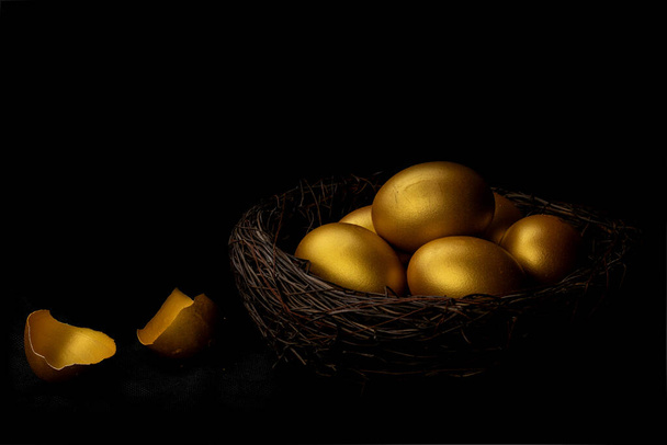 Zlaté vejce a skořápka v hnízdě izolované na černém pozadí - Fotografie, Obrázek