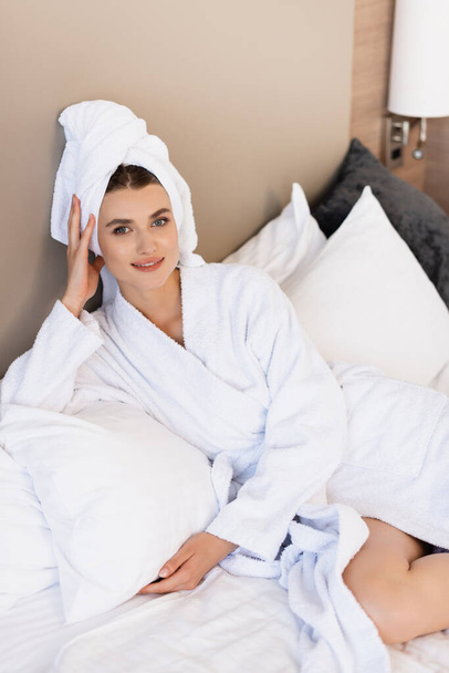 young woman in towel and white bathrobe lying on bed in hotel room  - Фото, изображение