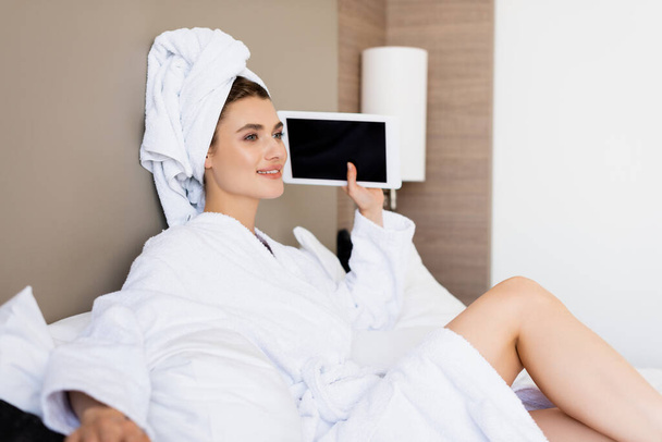 woman in towel and white bathrobe holding digital tablet with blank screen in hotel room - 写真・画像