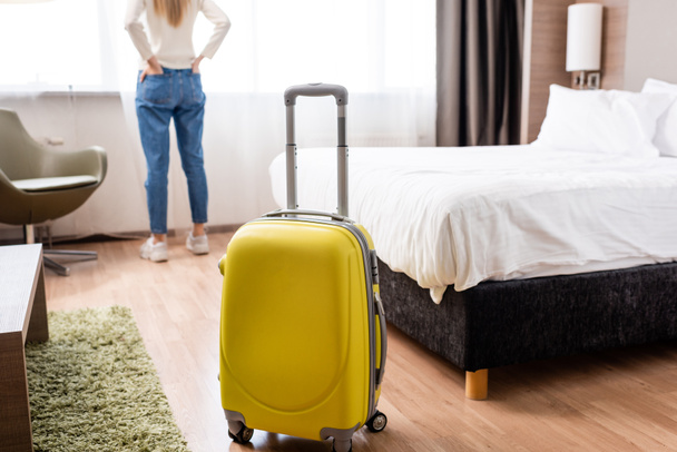 Gelbes Gepäckstück nahe Frau im Hotelzimmer im Fokus - Foto, Bild