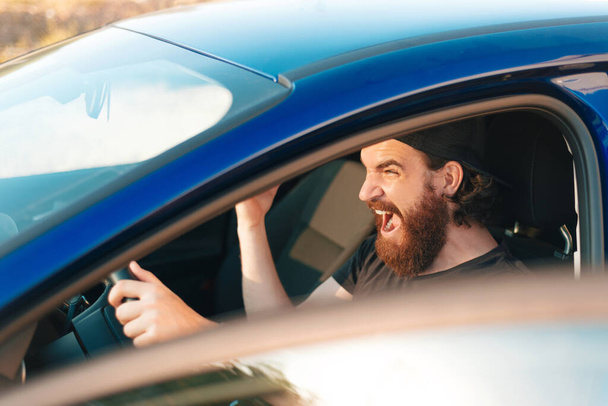 Foto ravvicinata di un autista arrabbiato con la barba che urla mentre si trova in mezzo al traffico - Foto, immagini